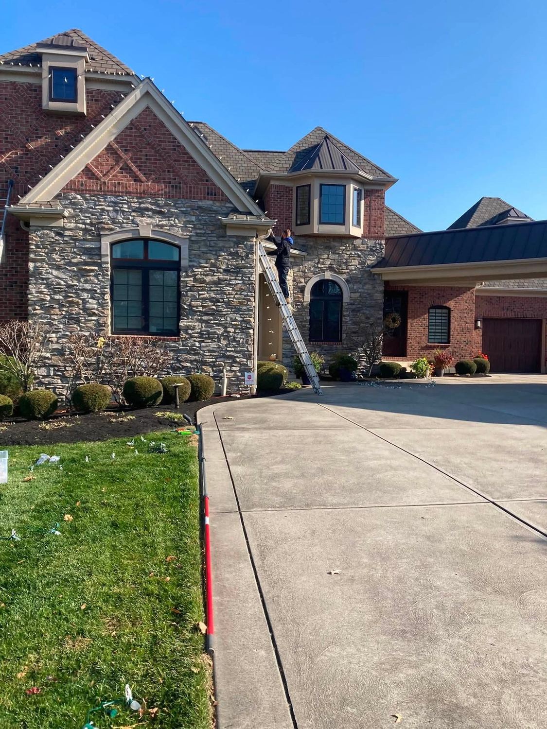 Stone frontage, ladder staged for the run — Christmas light installation by Mike’s Cincinnati Christmas Lights